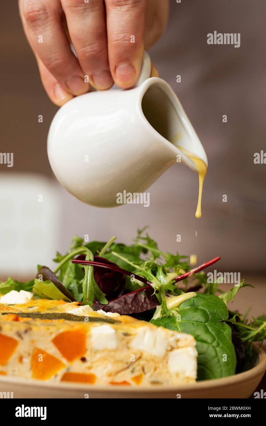 Nahaufnahme einer Person, die das Dressing auf einen Salat mit Babyblättern und Frittata in einem Café tröpfelt. Stockfoto