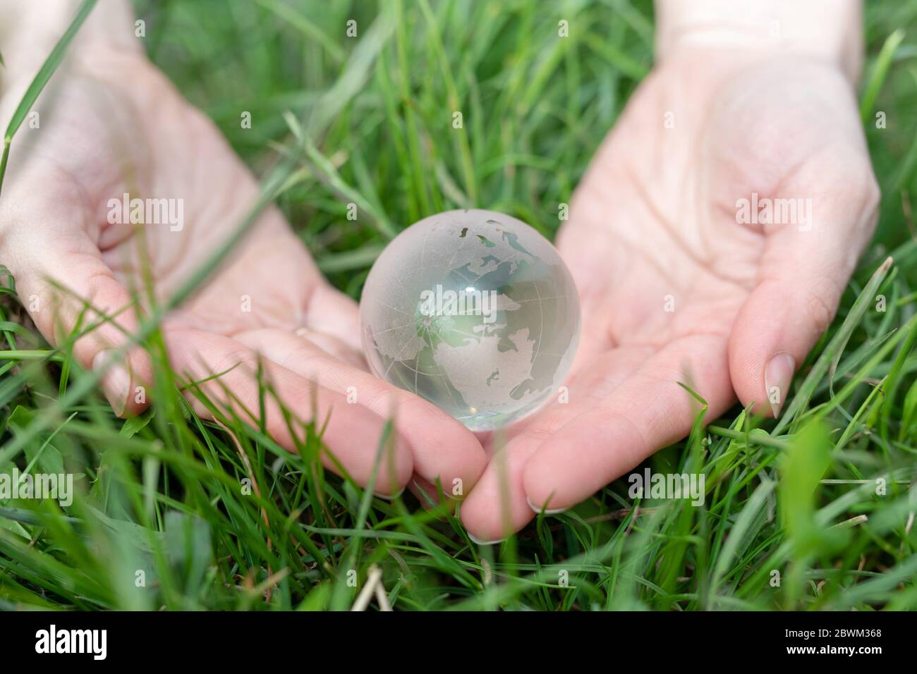 Planet Glaskugel in der menschlichen Hand auf Gras Hintergrund. Umwelt sparen, sauberen grünen Planeten retten, Ökologie Konzept. Stockfoto