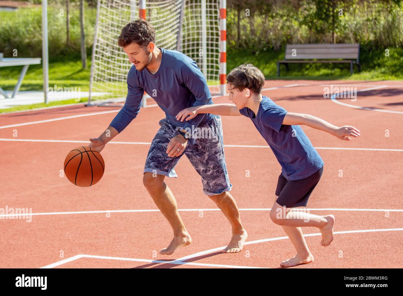 Vater und Sohn spielen barfuß Basketball auf einem Spielplatz Stockfoto