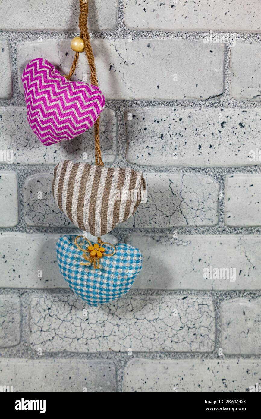 Drei Herzen auf einem Backstein Wand Hintergrund. Plüsch Herzen in rosa, braun und blau. Stockfoto