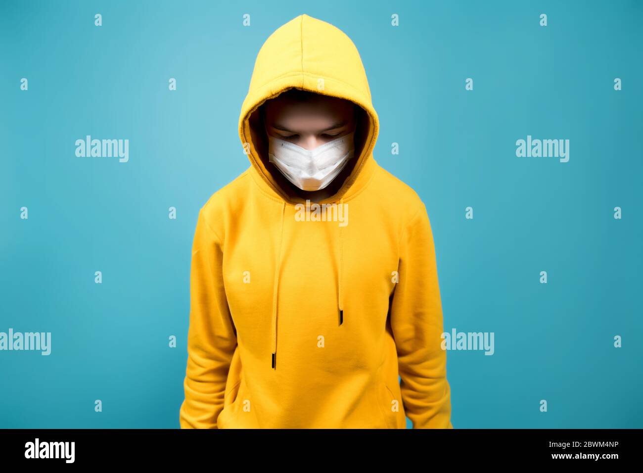 Ein junger Mann mit einem medizinischen Verband auf seinem Gesicht sieht nach unten. Blauer Hintergrund Stockfoto