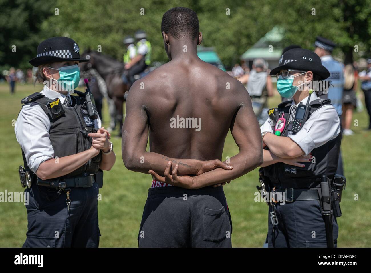 Coronavirus: Maskierte Polizisten befragen einen jungen schwarzen Mann im Hyde Park während eines illegalen Anti-Lockdown-Protests. Schwarze, asiatische und ethnische Minderheiten (BAME) Gemeinschaften wurden überproportional vom Coronavirus betroffen, während Boris Johnson derzeit unter Druck steht, die Ergebnisse einer Untersuchung sofort zu veröffentlichen, nachdem Vorwürfe erhoben wurden, dass sie wegen Befürchtungen, es könnte Rassenspannungen schüren, verzögert worden seien. London, Großbritannien. Stockfoto