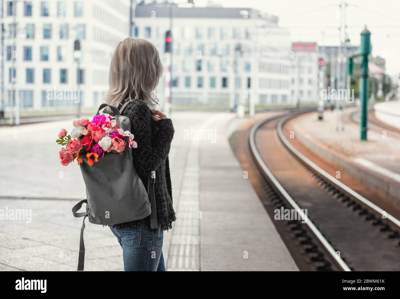 Junge Frau mit Rucksack mit Blumenstrauß wartet auf einen Zug. Foto von hinten. Stockfoto