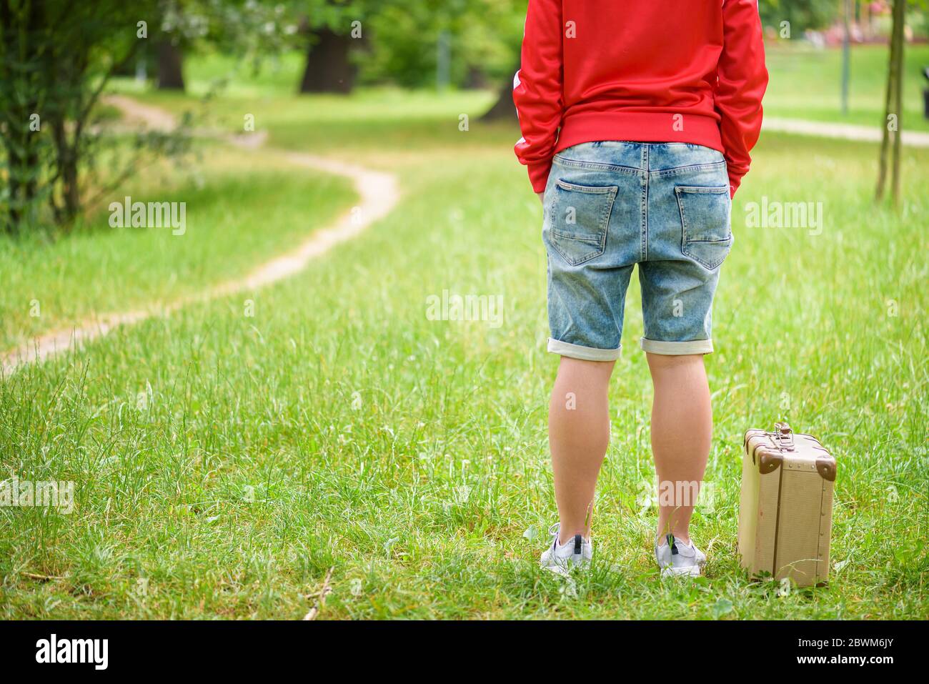Junge Person steht mit einem Vintage-Koffer. Foto von hinten. Lokales Reisekonzept Stockfoto