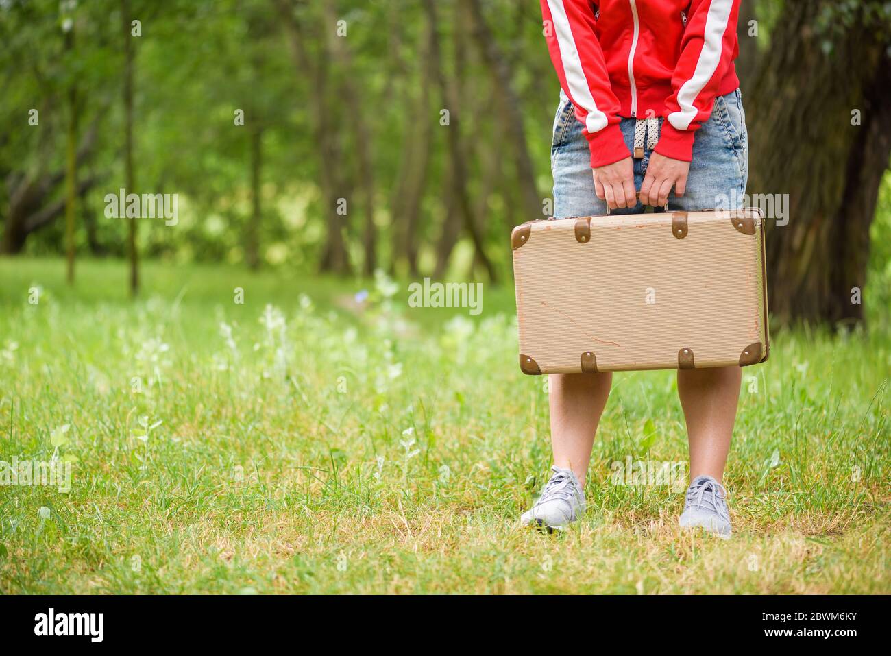 Junge Person steht mit einem Vintage-Koffer. Foto von hinten. Lokales Reisekonzept Stockfoto