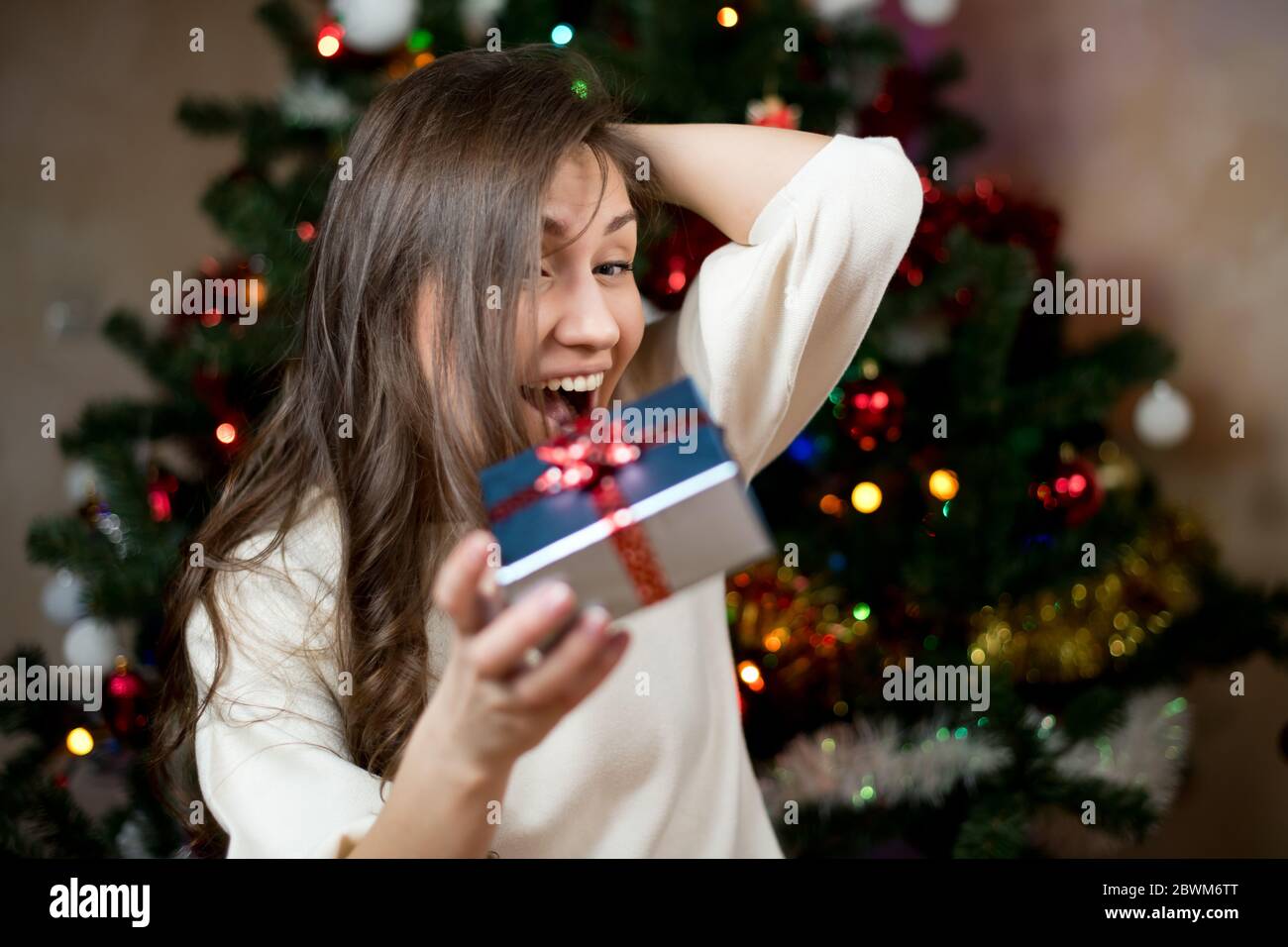 Mädchen freut sich hell in der Gabe für das neue Jahr. Vor dem Hintergrund des Weihnachtsbaums Stockfoto