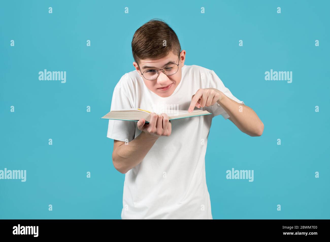 Nerd quetscht Schultern und schiebt ein Auge, zeigt einen Finger auf ein Buch Stockfoto