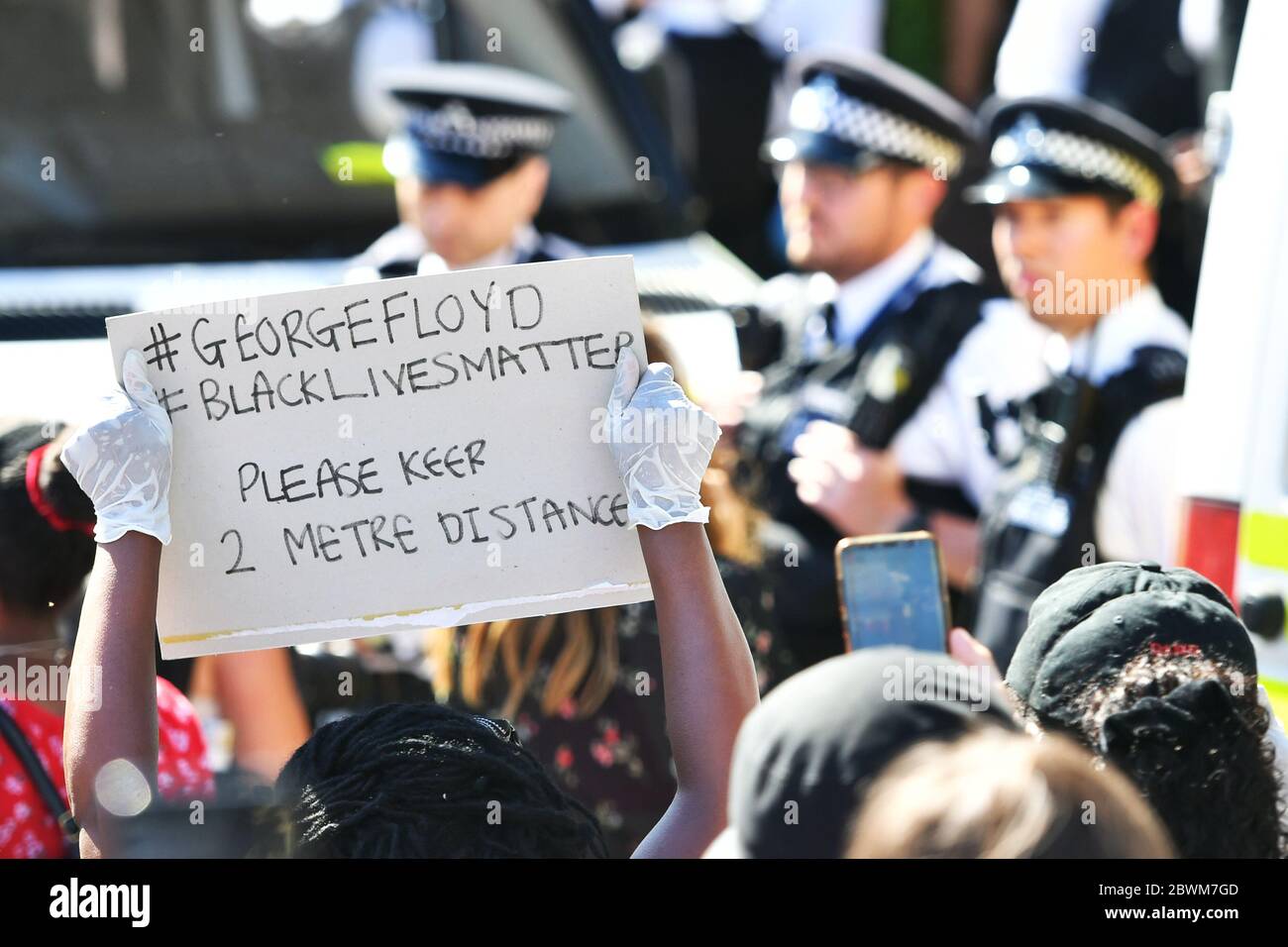 Ein Demonstrator hält ein Schild hoch, das die Menschen an soziale Distanz während eines Black Lives Matter Protests vor der US-Botschaft in London erinnert. Der Protest folgt dem Tod von George Floyd in Minneapolis, US, diese Woche, die einen Polizeibeamten gesehen hat, der mit Mord dritten Grades aufgeladen wird. Stockfoto