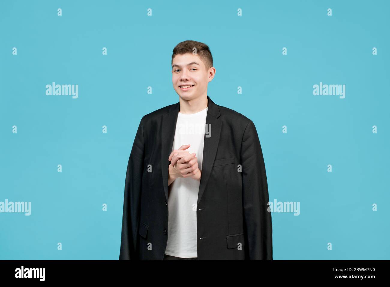 Ein Teenager in einer sehr großen Jacke lächelt schlau, die Hände gefeilt Stockfoto