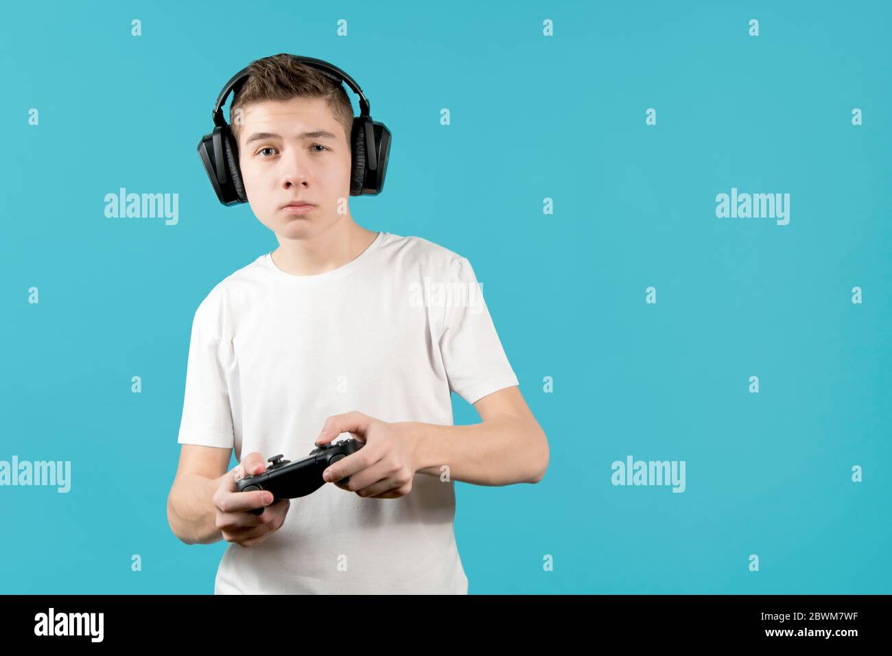 Teenager in Kopfhörer mit einem Joystick in den Händen. Copy Space, blauer Hintergrund Stockfoto