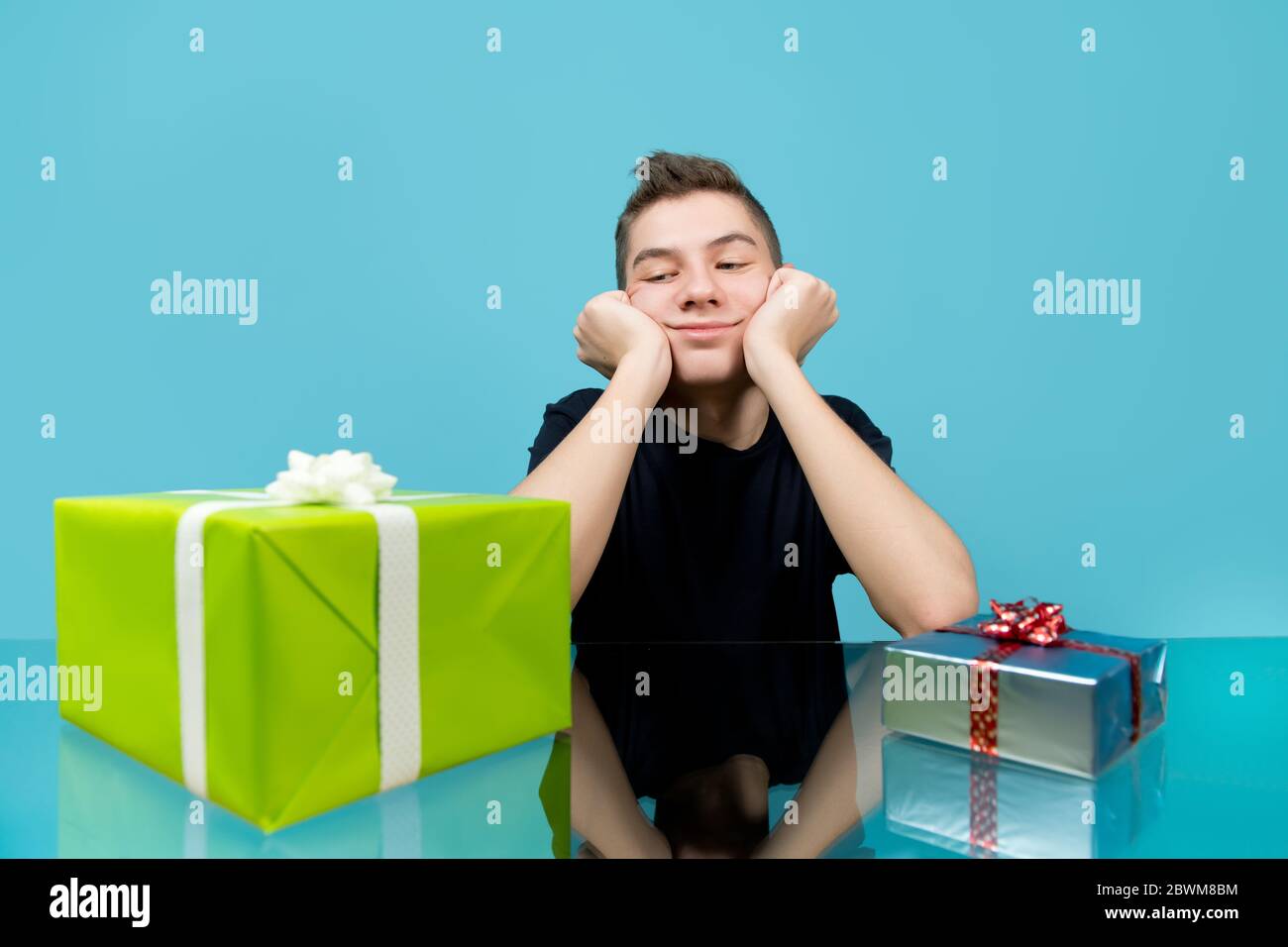 Junger Mann schaut auf ein großes Geschenk mit Vorfreude. Neben einem kleinen Geschenk liegt ein großes. Studio-Aufnahme, blauer Hintergrund Stockfoto