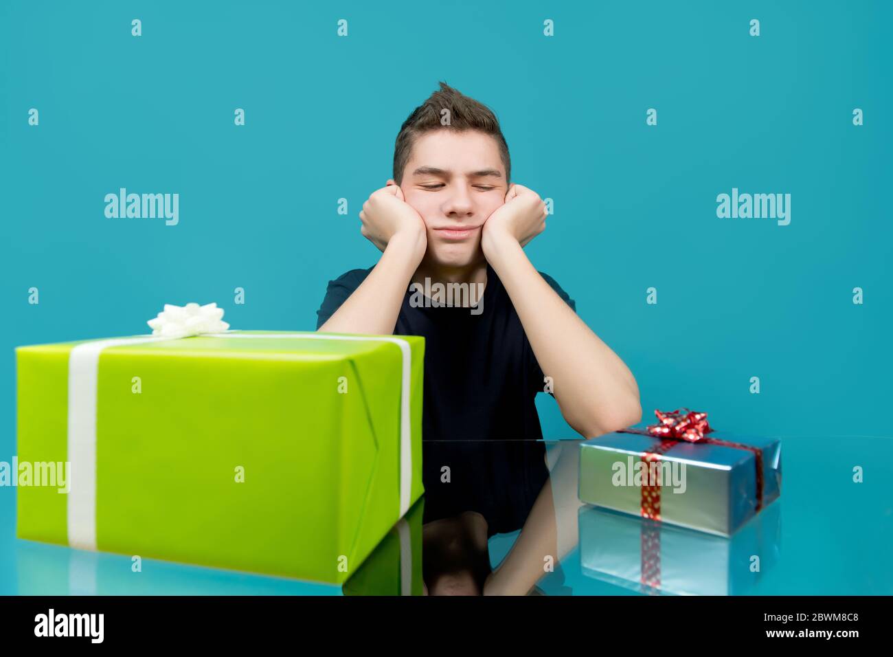 Ein Teenager ist verärgert, wenn er ein kleines Geschenk betrachtet, neben dem ein großes liegt. Blauer Hintergrund Stockfoto