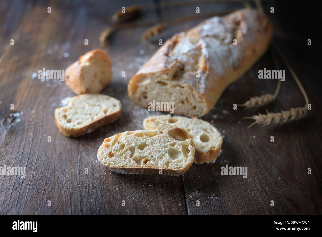 Frisches Baguette oder französisches Brot mit Zwiebeln gebacken, halb geschnitten, auf dunklem rustikalem Holz, ausgewählter Fokus, schmale Schärfentiefe Stockfoto