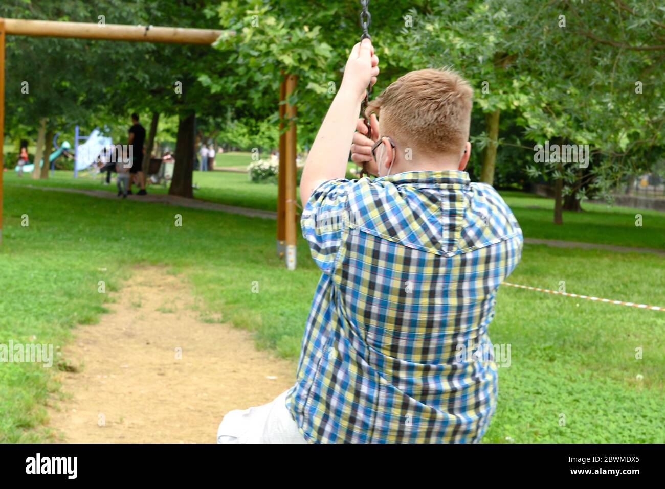 Junge mit chirurgischer Maske auf der Schaukel im Bereich von ​​the divetto durch ein rot-weiß gestreiftes Absperrband um den Spielplatz. Einzäunung rot und weiß Stockfoto