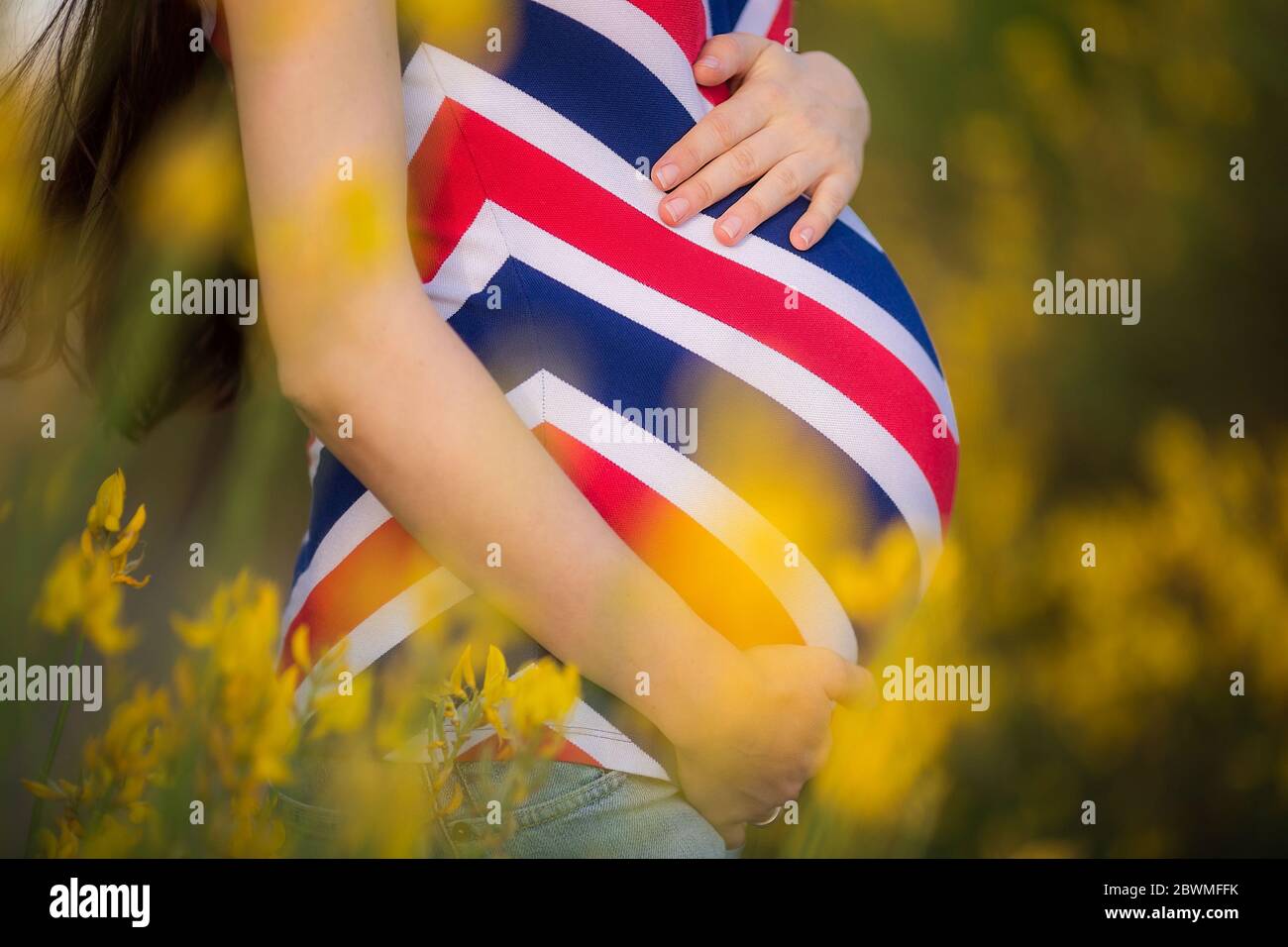 Schwangere Bauchnabelung. Junge schwangere Frau im Park mit gelben Blumen stehen. Mutterschaftskonzept. Platz für Text kopieren. Neues Lebenskonzept. Stockfoto