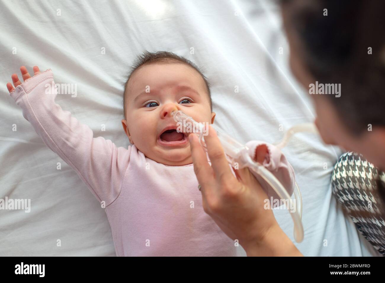 Nahaufnahme der fürsorglichen Mutter mit Nasenpumpe, um die Nase ihres Babys zu reinigen. Baby liegt im Bett Stockfoto