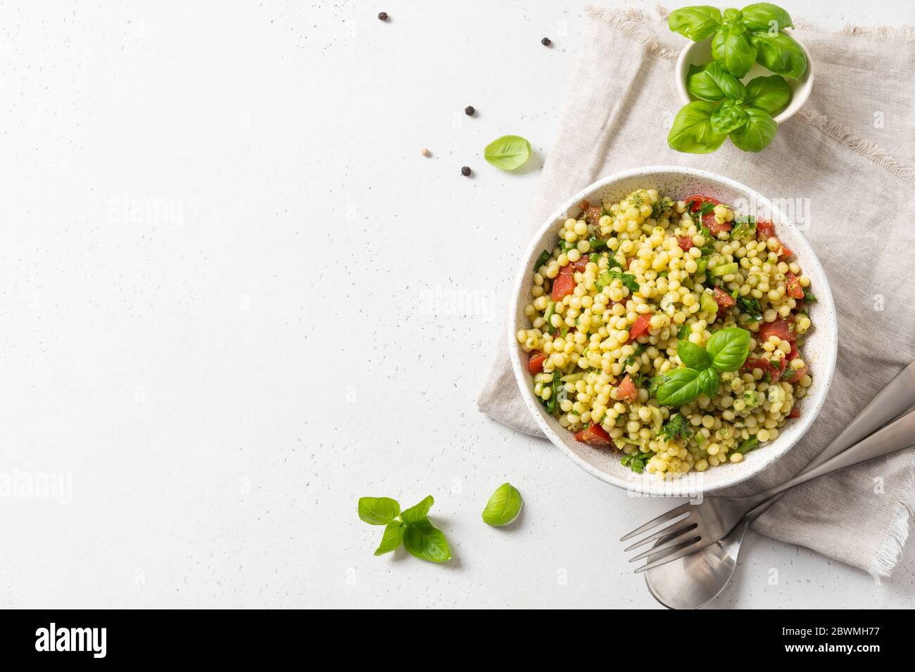 Gemüsesalat mit Pasta Ptitim oder Birdy, israelisch Couscous dekoriert Basilikumblätter auf weißem Hintergrund. Draufsicht. Stockfoto