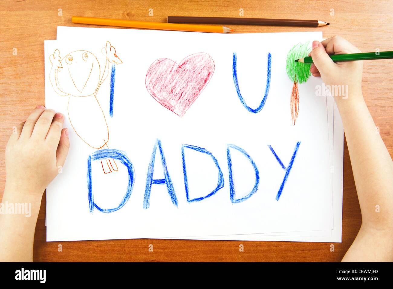 Das Konzept des Vatertags. Childs Hände Zeichnung Karte mit Worten I Love U Papa, und rotes Herz, und Farbstifte auf Holztisch. Stockfoto