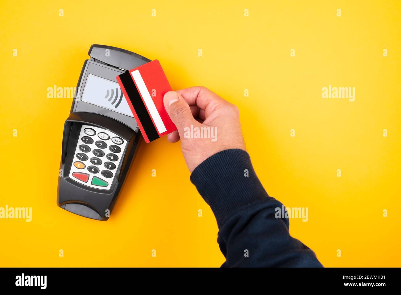 Kontaktloses Bezahlkonzept, direkt über Ansicht der Person, die Kreditkarte oder Debitkarte gegen POS-Zahlungsterminal auf orangefarbenem Hintergrund hält Stockfoto