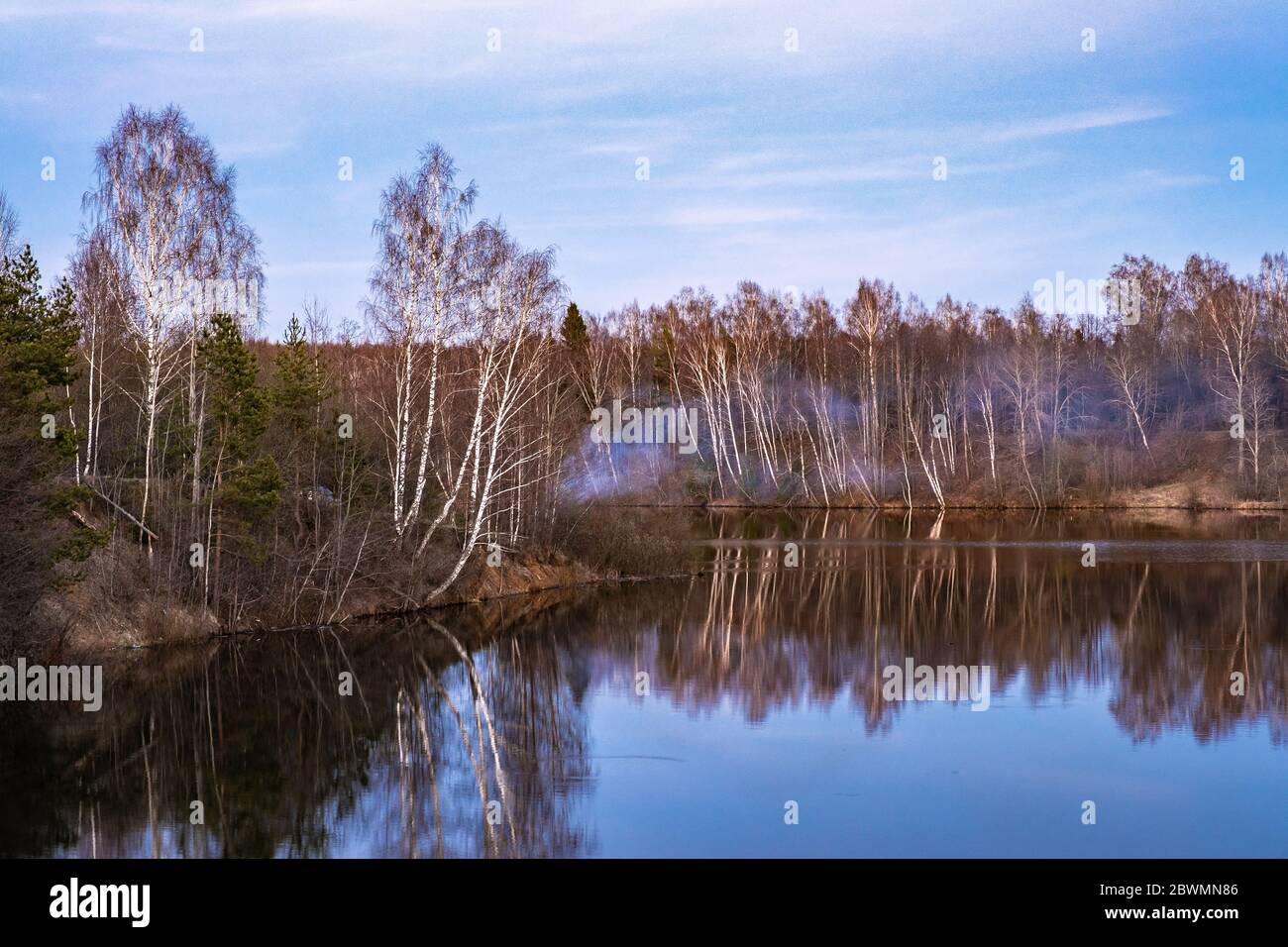 Ein steiles Ufer mit Bäumen und Büschen, der Uvod Fluss und der blaue Rauch eines Lagerfeuers an einem ruhigen Abend, Russland überwuchert. Stockfoto