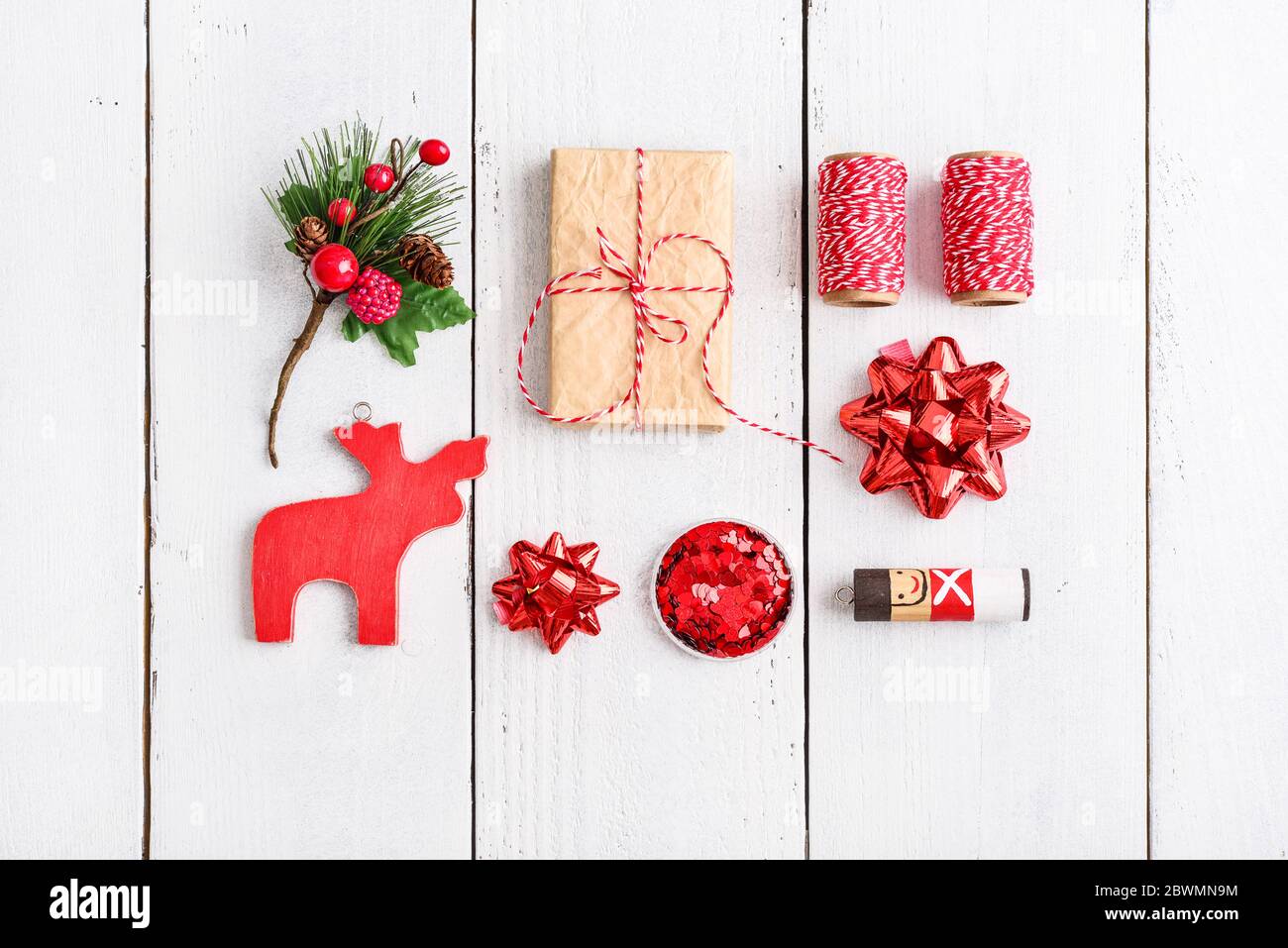 Weihnachts-Set: Geschenkbox, rote Schleife, Weihnachtsdekor, Funkeln, Band zum Verpacken von Geschenken auf weißem Holzhintergrund, Draufsicht. Stockfoto