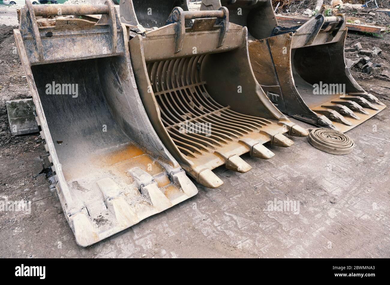 Große gebrauchte Baggerschaufeln stehen nebeneinander auf einem Zementboden. Stockfoto