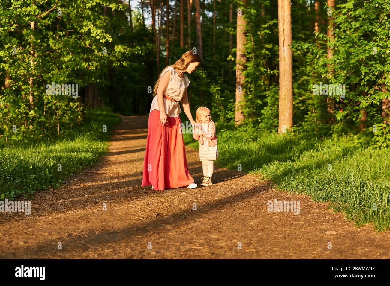 Mutter und Tochter gehen den Weg im Abendpark entlang, Mädchen schaut sich mit Besorgnis um Stockfoto
