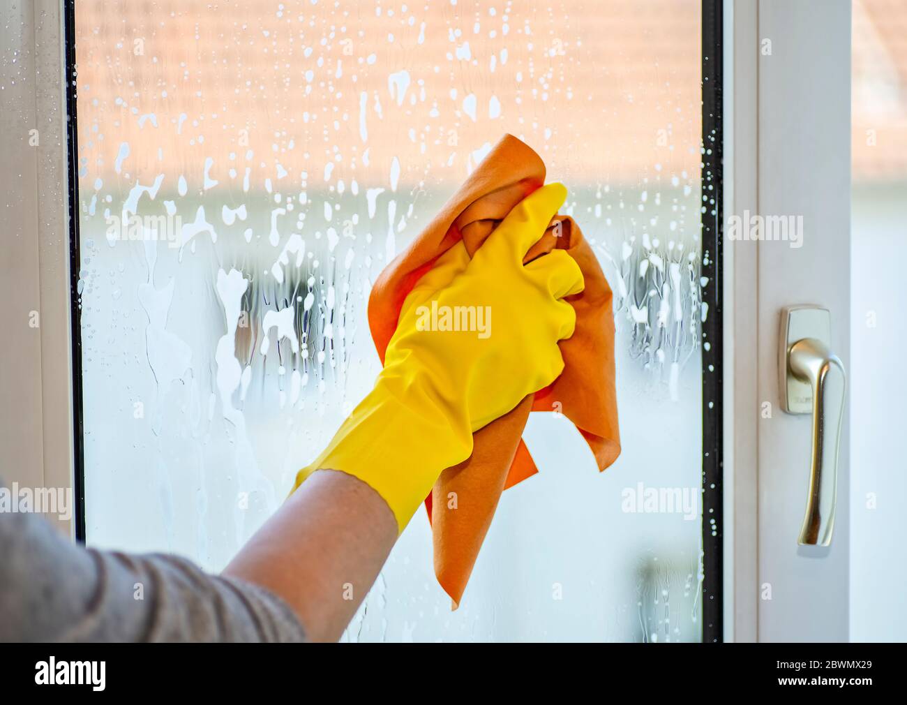 Hand mit gelbem Gummihandschuh und Tuch beim Reinigen eines Fensters Stockfoto