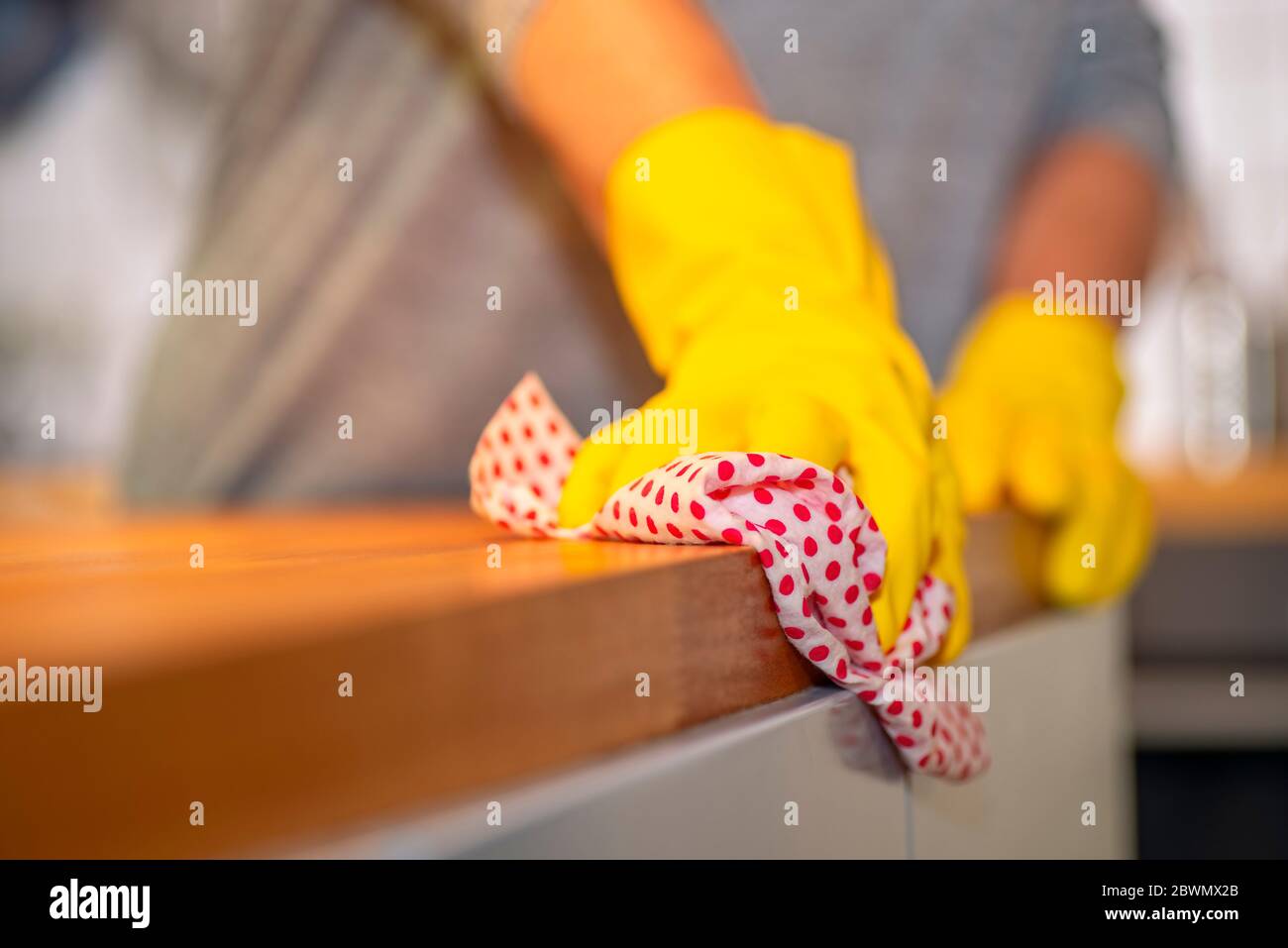 Person mit gelben Gummihandschuhen wischt mit einem Tuch über eine Arbeitsplatte in einer Küche Stockfoto