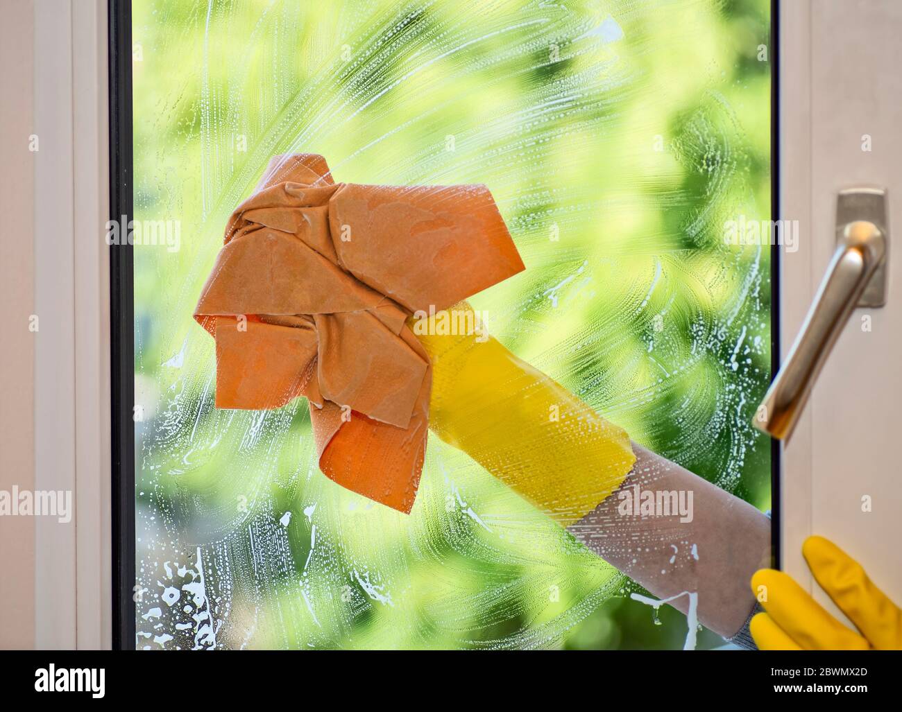 Hand mit gelbem Gummihandschuh und Tuch beim Reinigen eines Fensters Stockfoto
