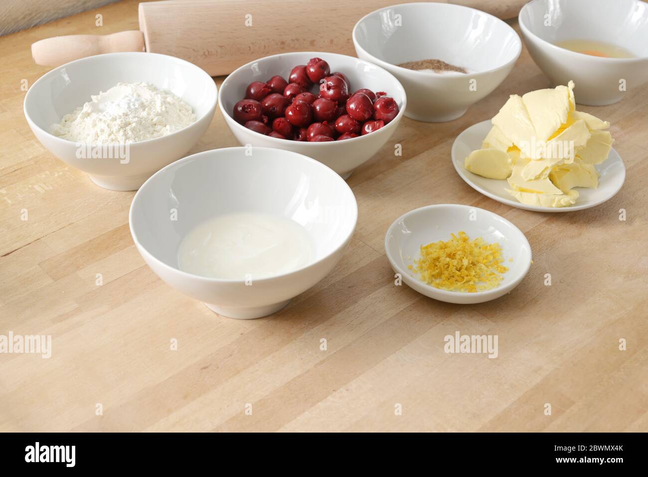 Backen zu Hause, Zutaten in weißen Schalen für einen Kirschkuchen auf einer hölzernen Küchenarbeitspfläche, Kopierfläche, ausgewählter Fokus, schmale Schärfentiefe Stockfoto