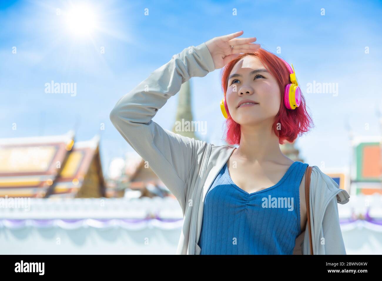 Asiatische Mädchen teen rote Haare gefärbt stehen im Freien gegen hohe UV-Sonne Licht im Sommer Saison sonnigen Tag Himmel Thai Tempel Hintergrund. Stockfoto