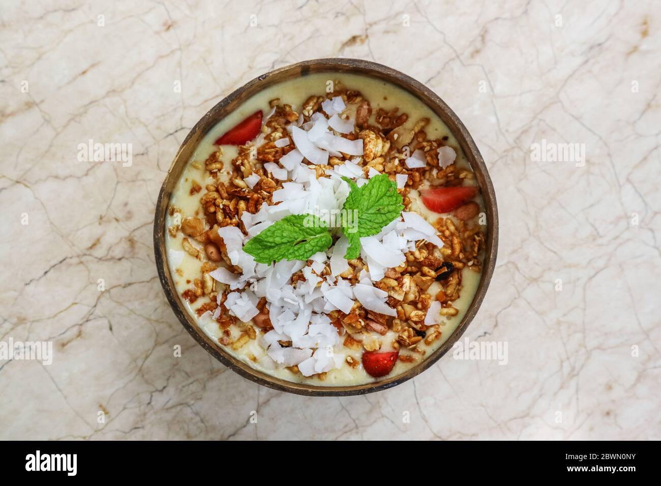 Smoothie Schüssel mit Mango, Joghurt, Müsli und Erdbeere in Kokosnussschale Schüssel auf hellem Hintergrund, Draufsicht Stockfoto