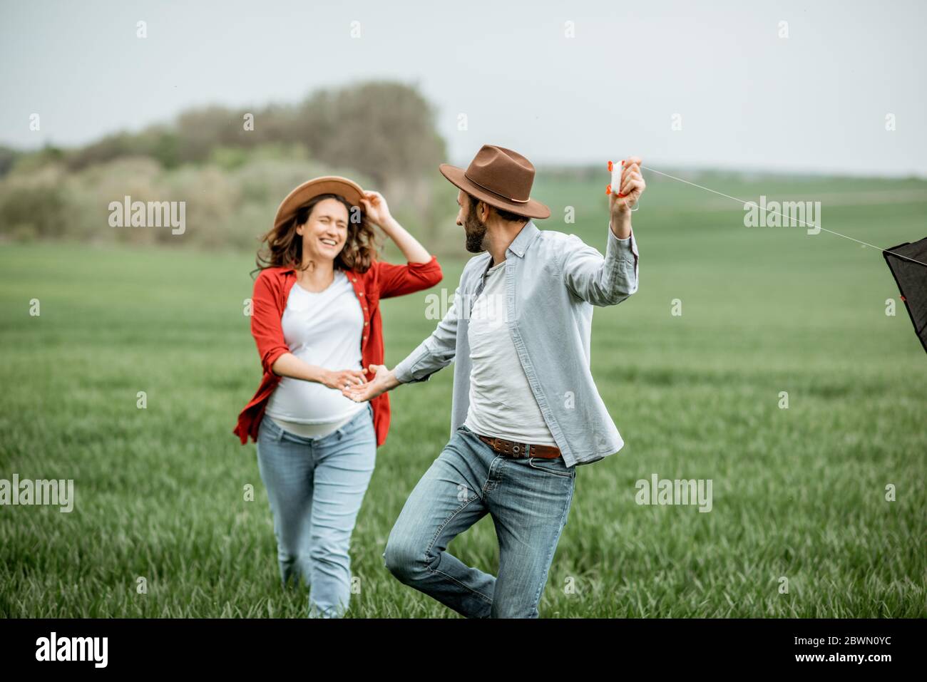 Glückliches Paar, das Spaß zusammen hat, mit Drachen auf dem Greenfield spielt. Glückliches Paar erwartet ein Baby und junge Familie Konzept Stockfoto