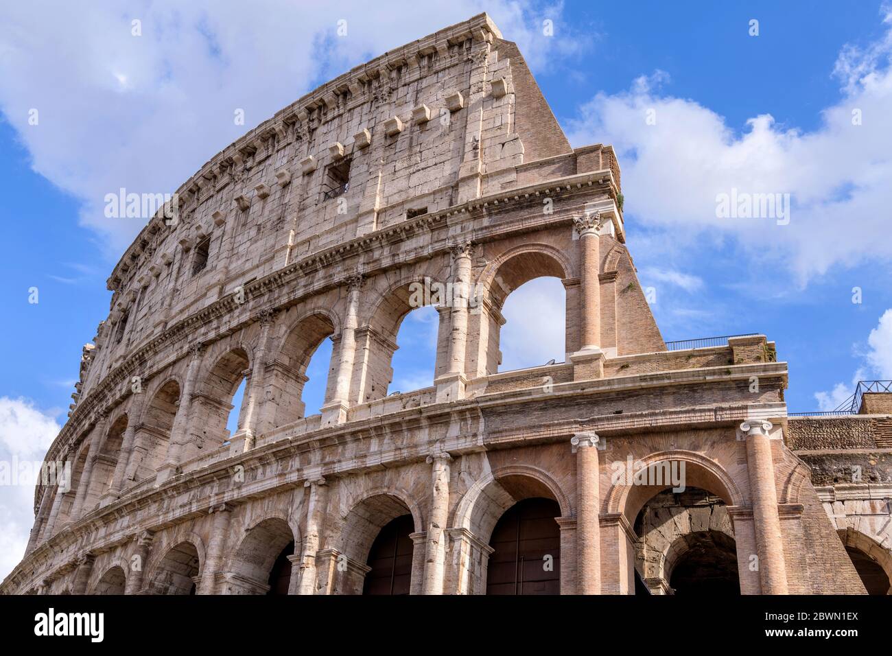 Wand des Kolosseums - Nahaufnahme des oberen Teils der westlichen Außenwand des Kolosseums, gegen weiße Wolken und blauen Himmel. Rom, Italien. Stockfoto