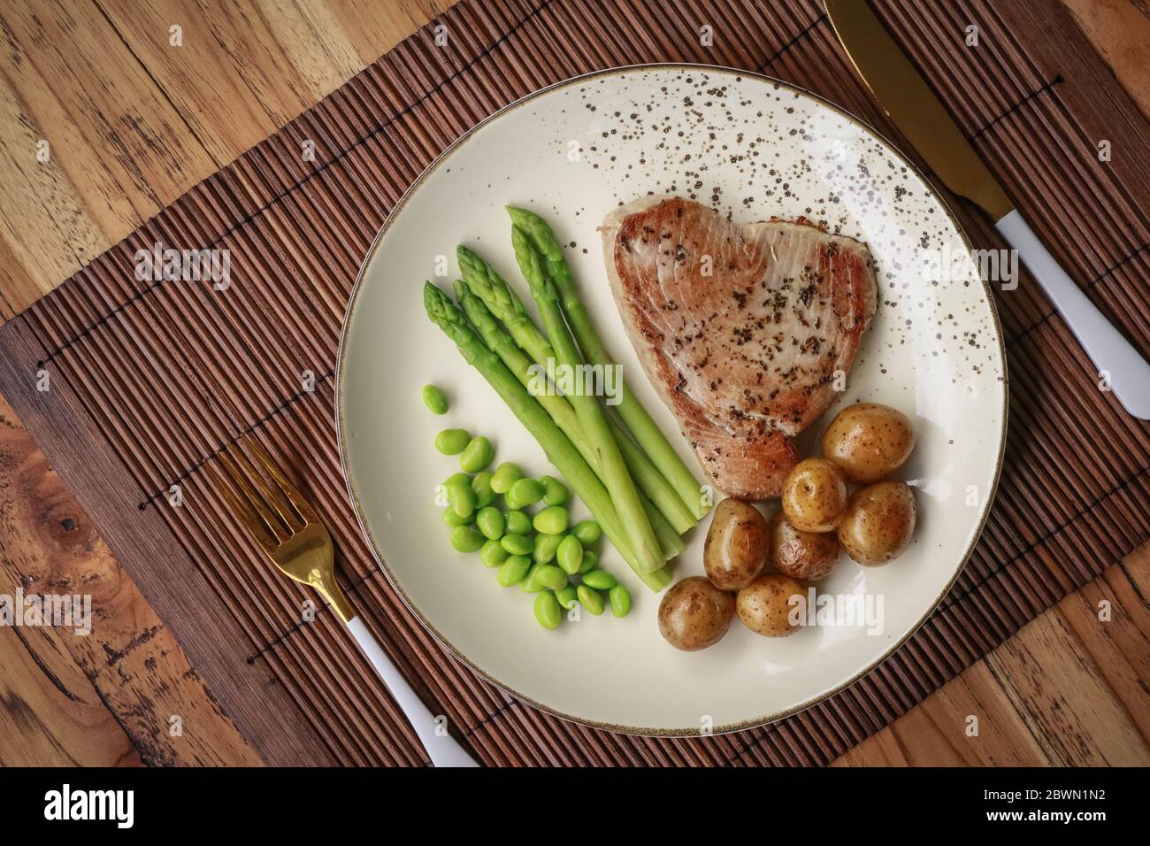 Gegrilltes Thunfischsteak mit Spargel, gebratenen Babykartoffeln, Edamamebohnen und Sauce Hollandaise auf einem Teller, Draufsicht Stockfoto