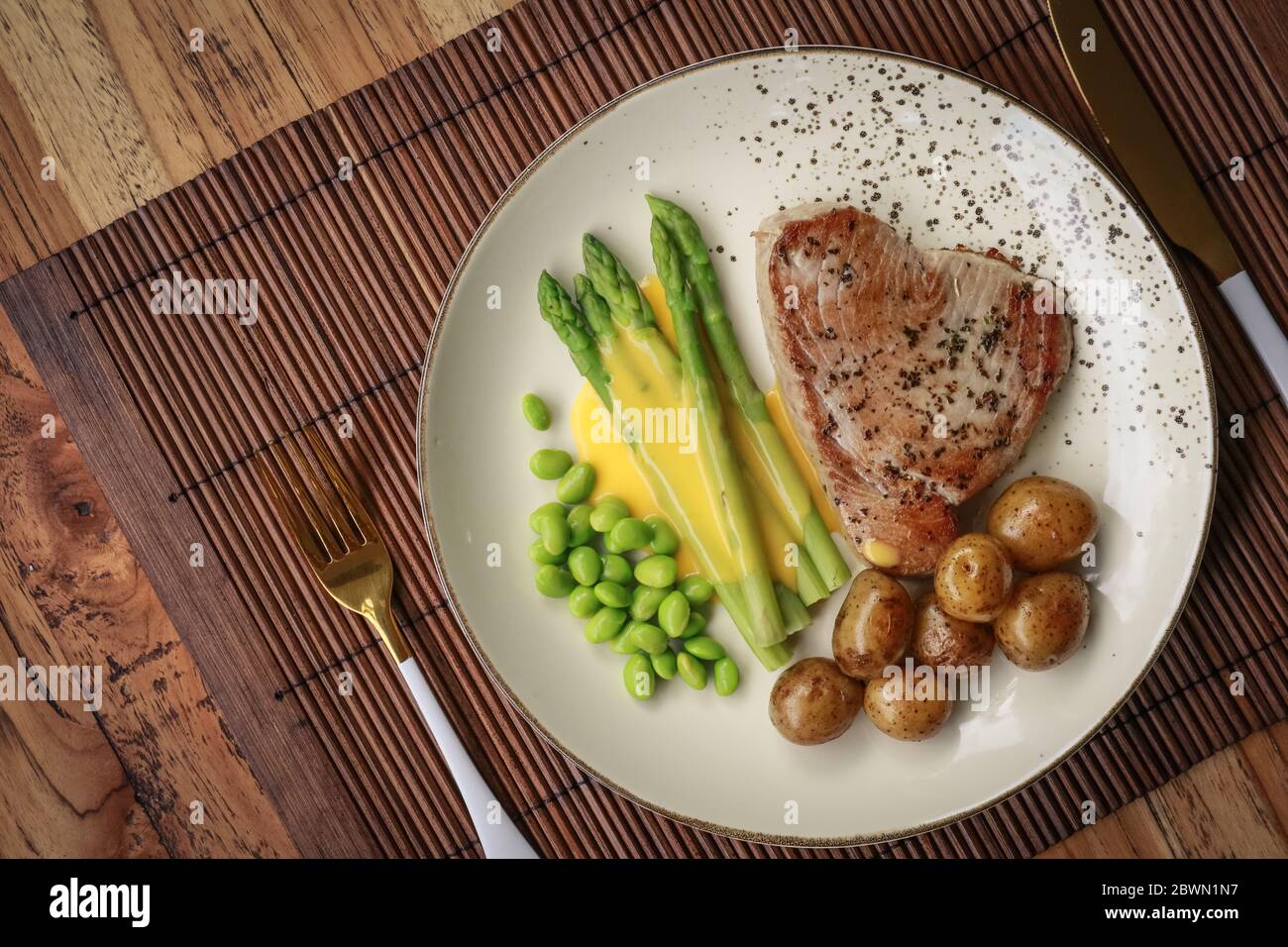 Gegrilltes Thunfischsteak mit Spargel, gebratenen Babykartoffeln, Edamamebohnen und Sauce Hollandaise auf einem Teller, Draufsicht Stockfoto