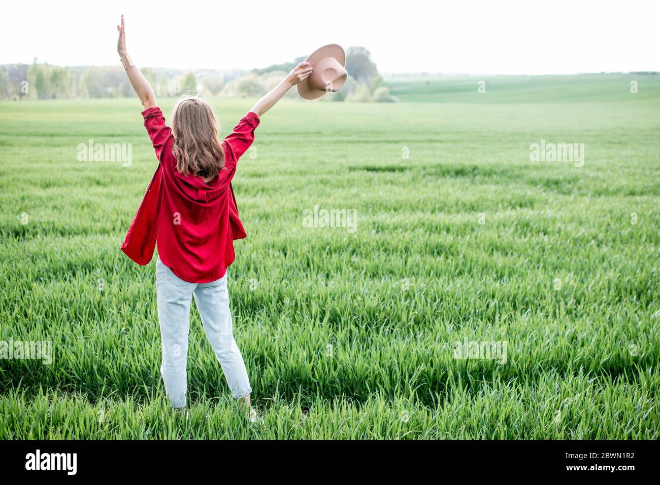 Stilvolle Frau genießen Frühling und Natur auf dem grünen Feld, Rückansicht. Konzept eines unbeschwerten Lebensstils und Freiheit Stockfoto