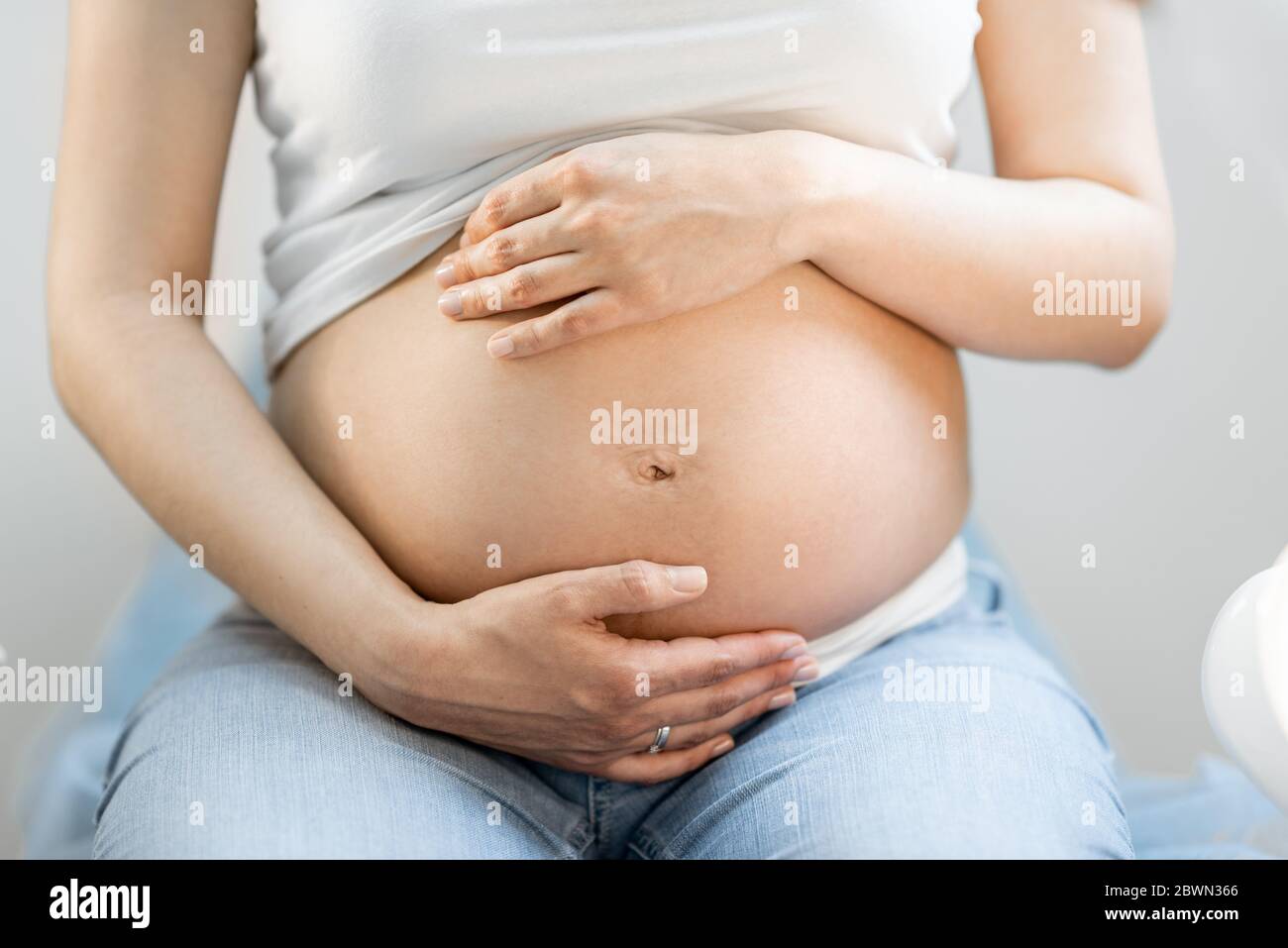 Schwangere Frau umarmt ihren Bauch, sitzt auf einem gynäkologischen Stuhl  während einer medizinischen Untersuchung, beschnitten Ansicht ohne Gesicht  auf Bauch konzentriert Stockfotografie - Alamy