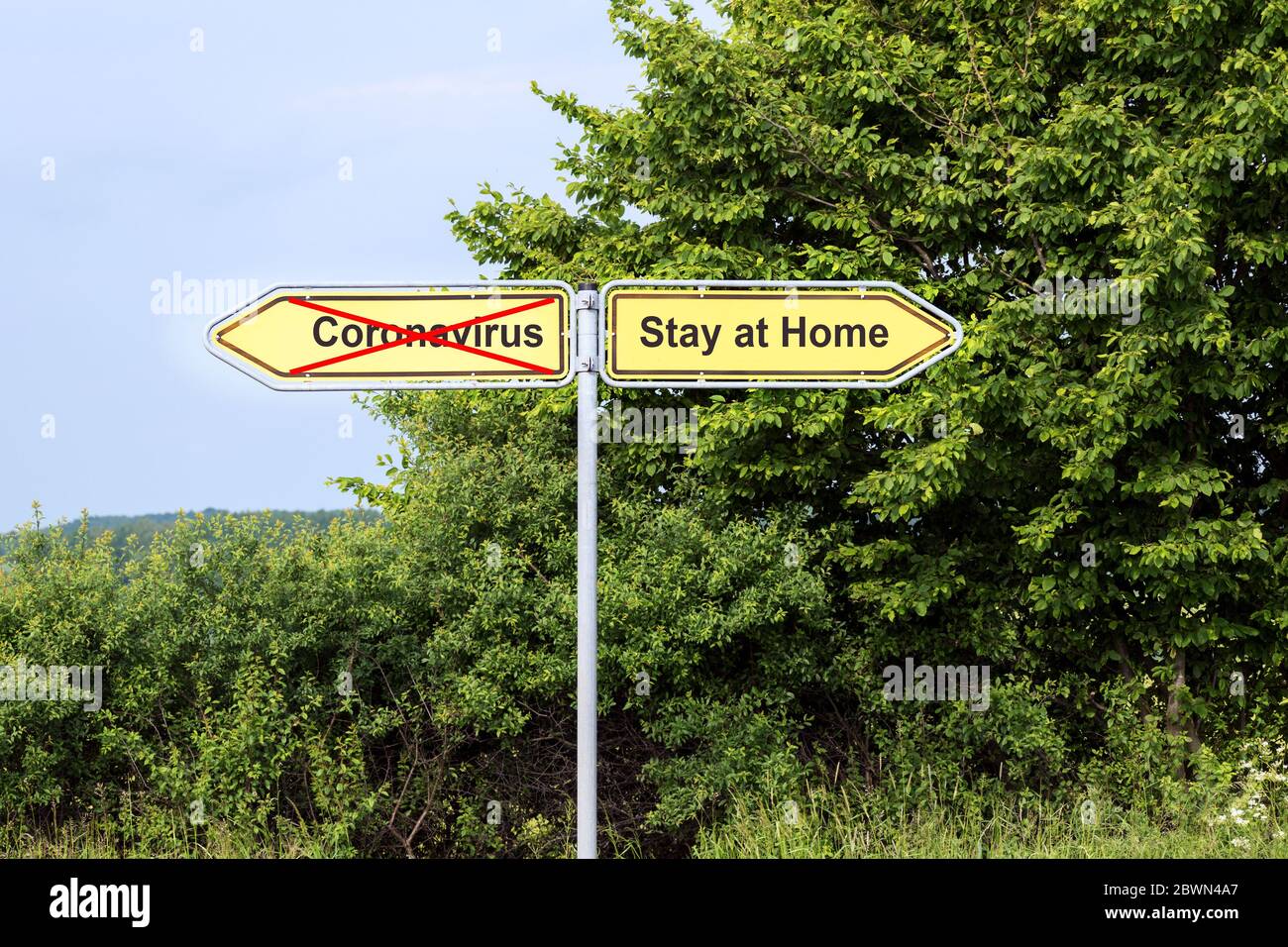 Gelbe Straßenschilder zeigen in entgegengesetzte Richtungen mit Text Coronavirus und Aufenthalt zu Hause, ländliche Landschaft im Hintergrund, Gesundheitskonzept durin Stockfoto