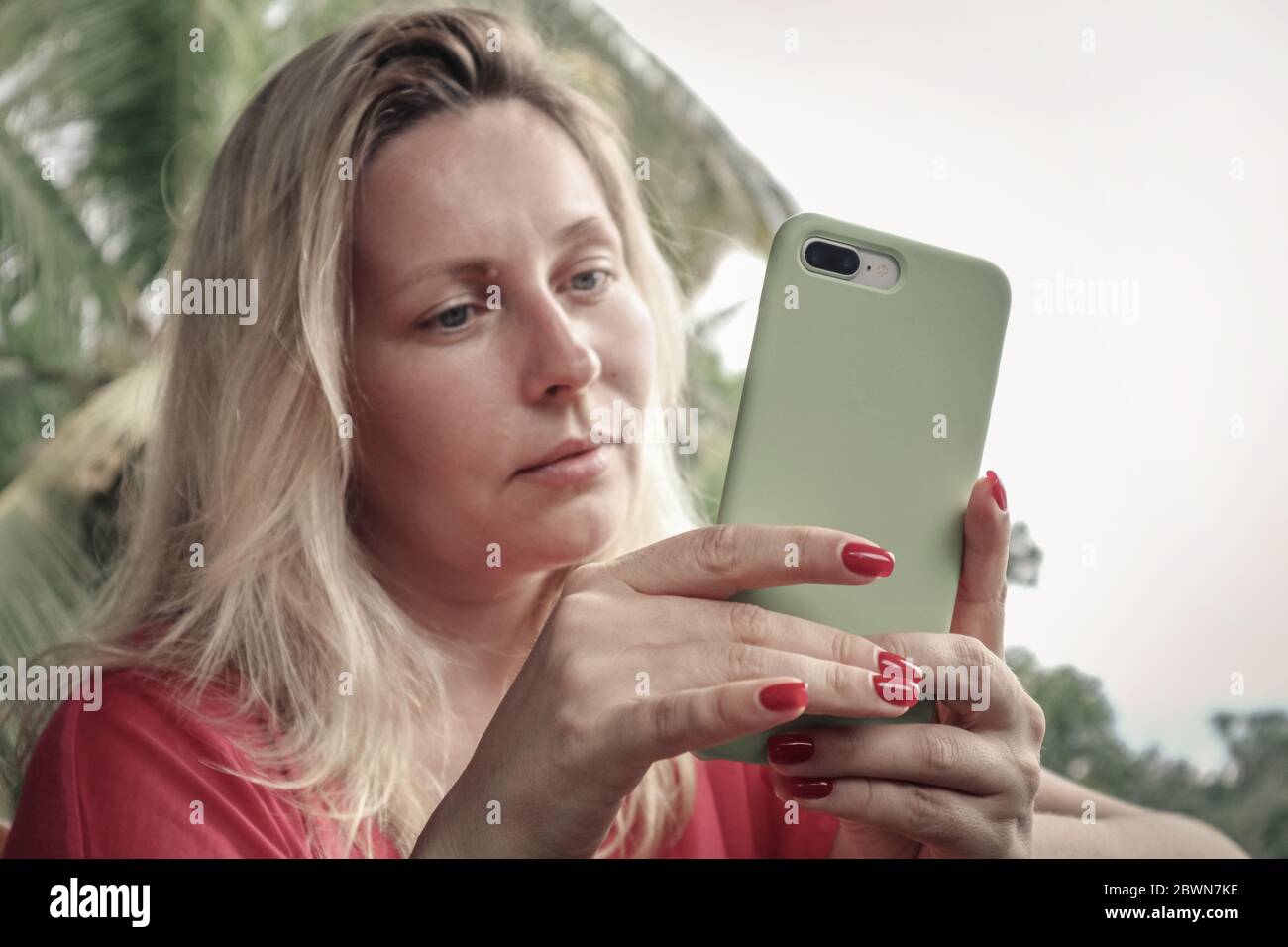 Erwachsene blonde Frau hält , mit und Blick auf Smartphone im Freien auf Bali Insel, Indonesien. Stockfoto