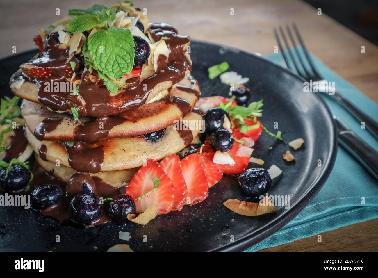 Pfannkuchen mit Banane, Heidelbeeren, Erdbeeren und Schokoladensauce auf einem Teller Nahaufnahme Stockfoto