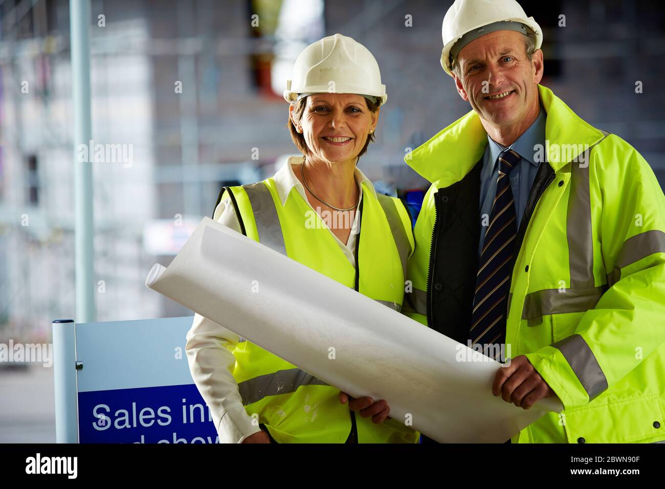 Porträt von zwei reifen Architekten in Schutzkleidung auf der Baustelle Blick auf Kamera hält eine Blaupause Stockfoto
