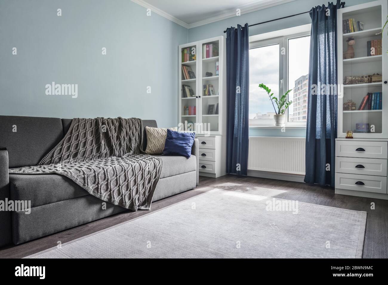 Helles, gemütliches Teenagerzimmer mit weißen Bücherregale, grauem Sofa und blauen Wänden Stockfoto