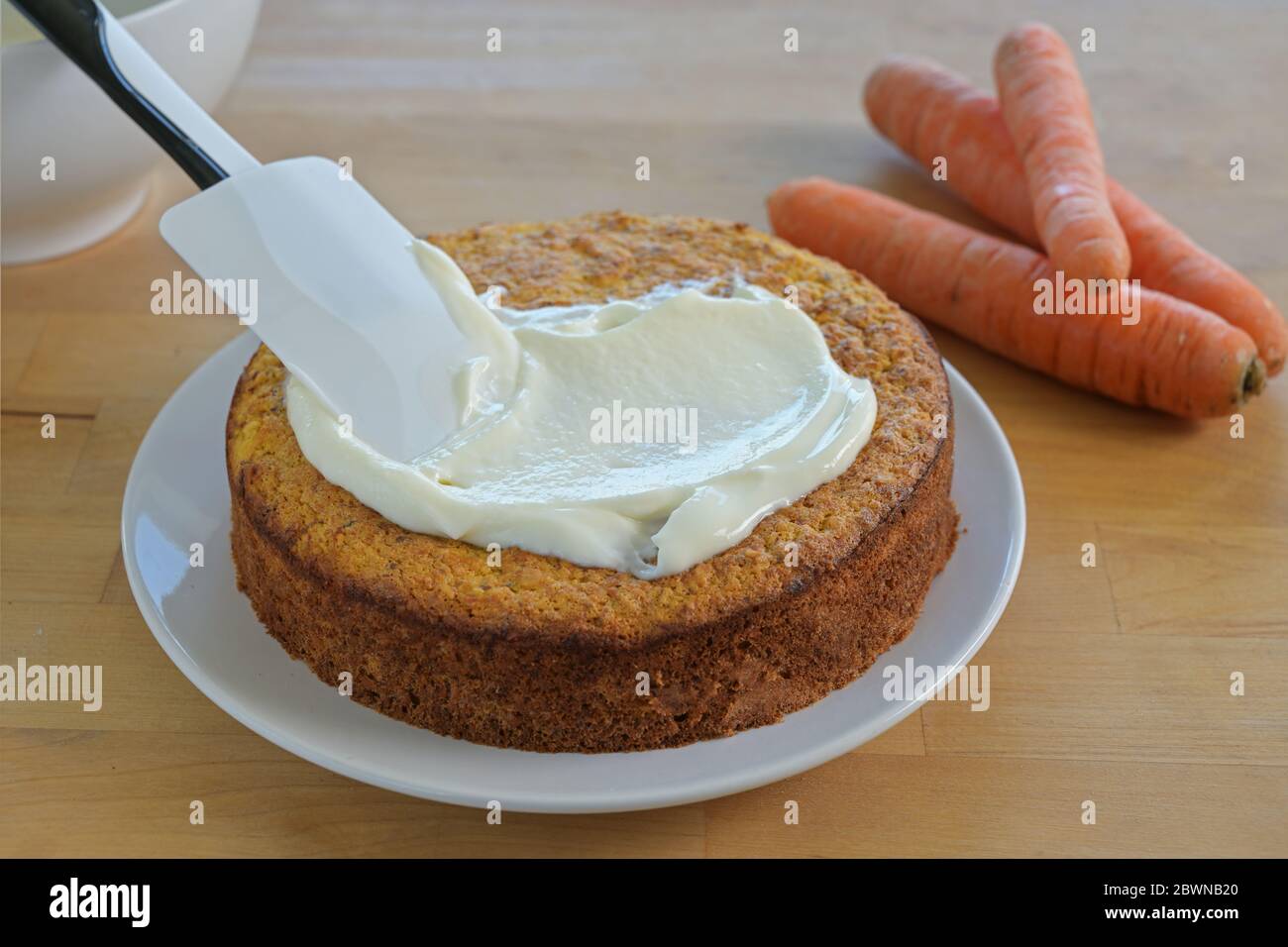 Verteilen Zuckerguss auf einem frisch gebackenen Karottenkuchen, Holztisch, ausgewählten Fokus, schmale Schärfentiefe Stockfoto