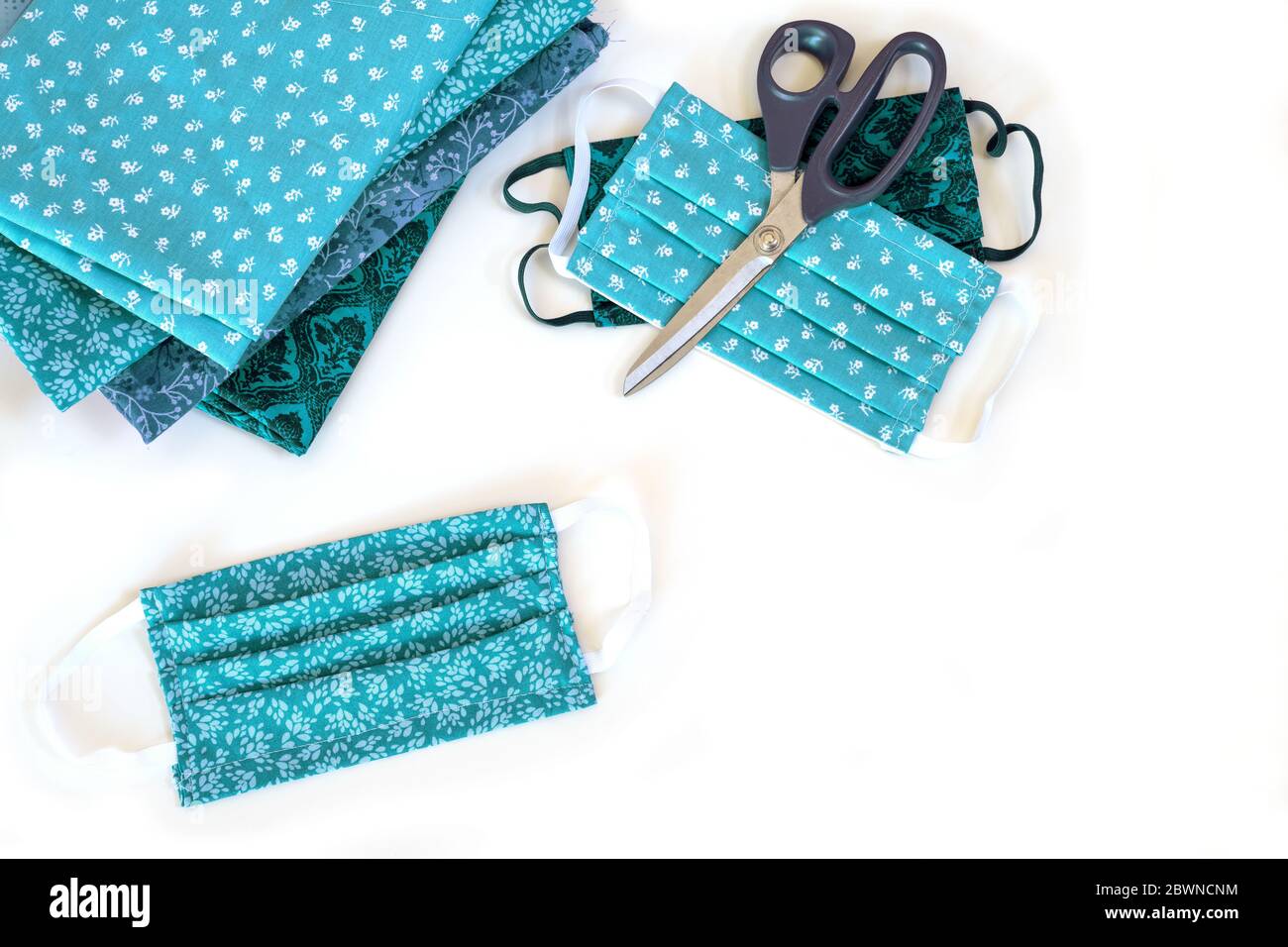 Hausgemachte Community Gesichtsmaske, Schere und Baumwollstoff auf einem weißen Tisch, Nähen während der Coronavirus-Pandemie, weil chirurgische Masken sind kurz Stockfoto