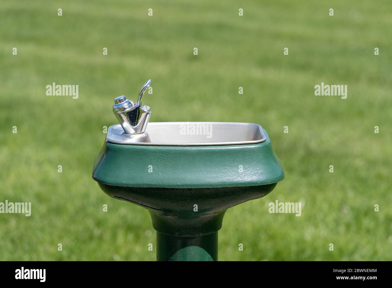 Trinkwasserbrunnen im Freien in einem Park mit Bokeh Gras dahinter. Während das Wasser selbst sicher ist, müssen die Oberflächen, die von anderen berührt werden könnten b Stockfoto