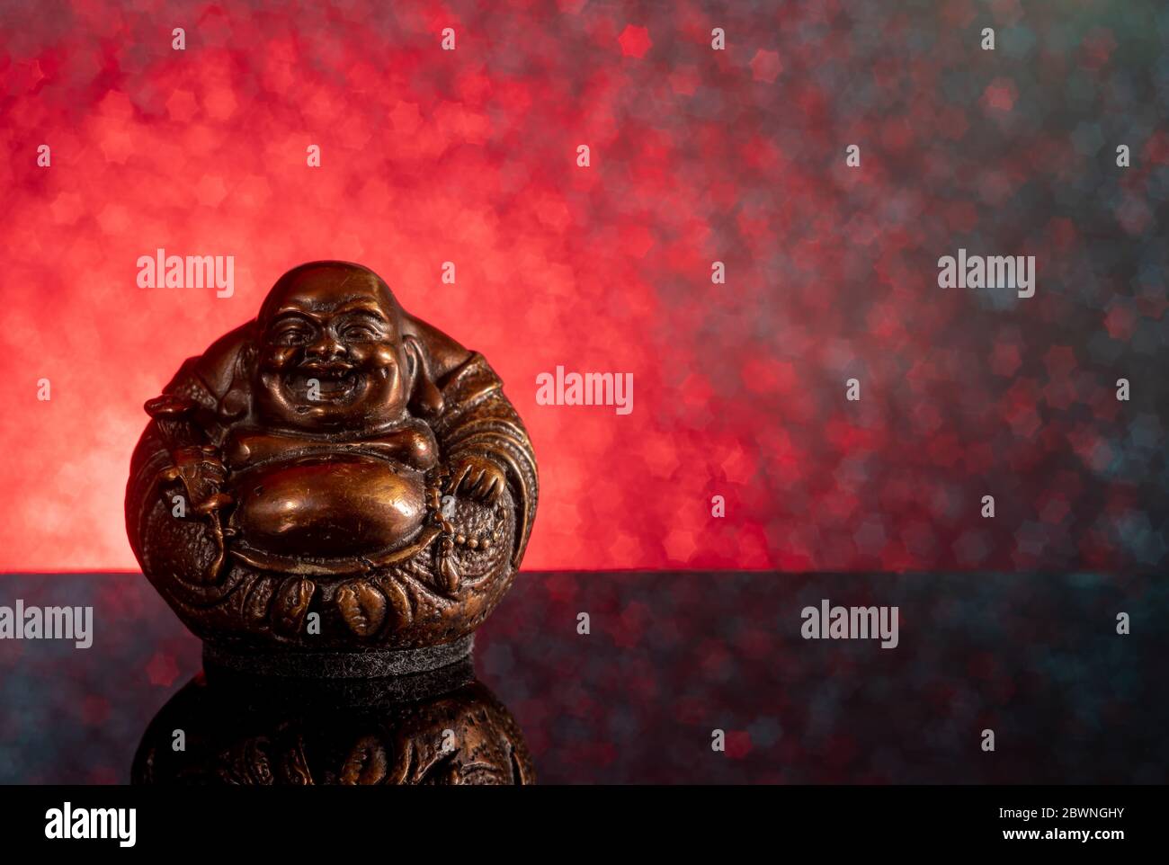 Chinesisch lachender buddha Hotei oder Budai auf einem rot-schwarzen Hintergrund mit Sternen und Spiegelung Stockfoto
