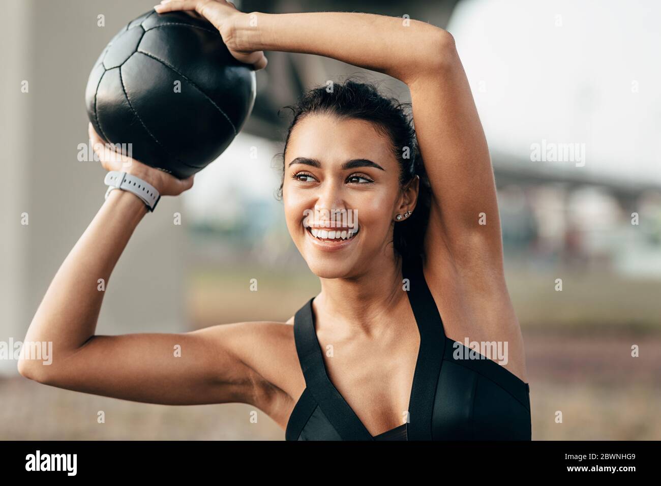 Lächelnde Frau in Sportkleidung, die Fitness-Training mit einem Medizinball Stockfoto