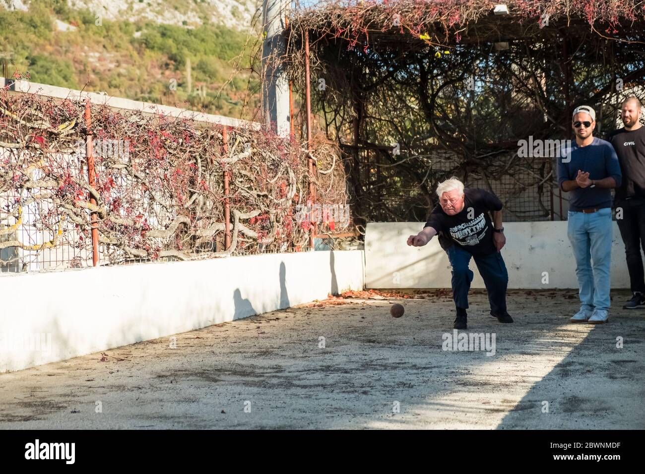 Ein älterer Mann wirft einen Bowling-Ball, während 2 jüngere Männer auf einer Freibahn in Dalmatien, Kroatien, schauen Stockfoto